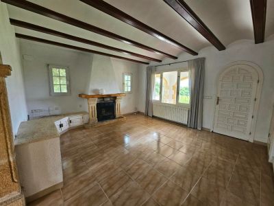 Living room with stone fireplace, wood beams, and tile flooring.