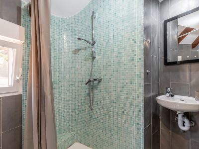 Bathroom detail with turquoise mosaic shower, wall-mounted sink, and gray tiled walls.