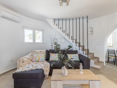Bright living room featuring a gray sofa, stone staircase with black railing, and light wood coffee table.