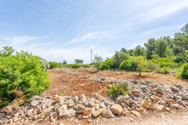 View of the plot featuring a stone wall and reddish soil, ideal for building close to nature.