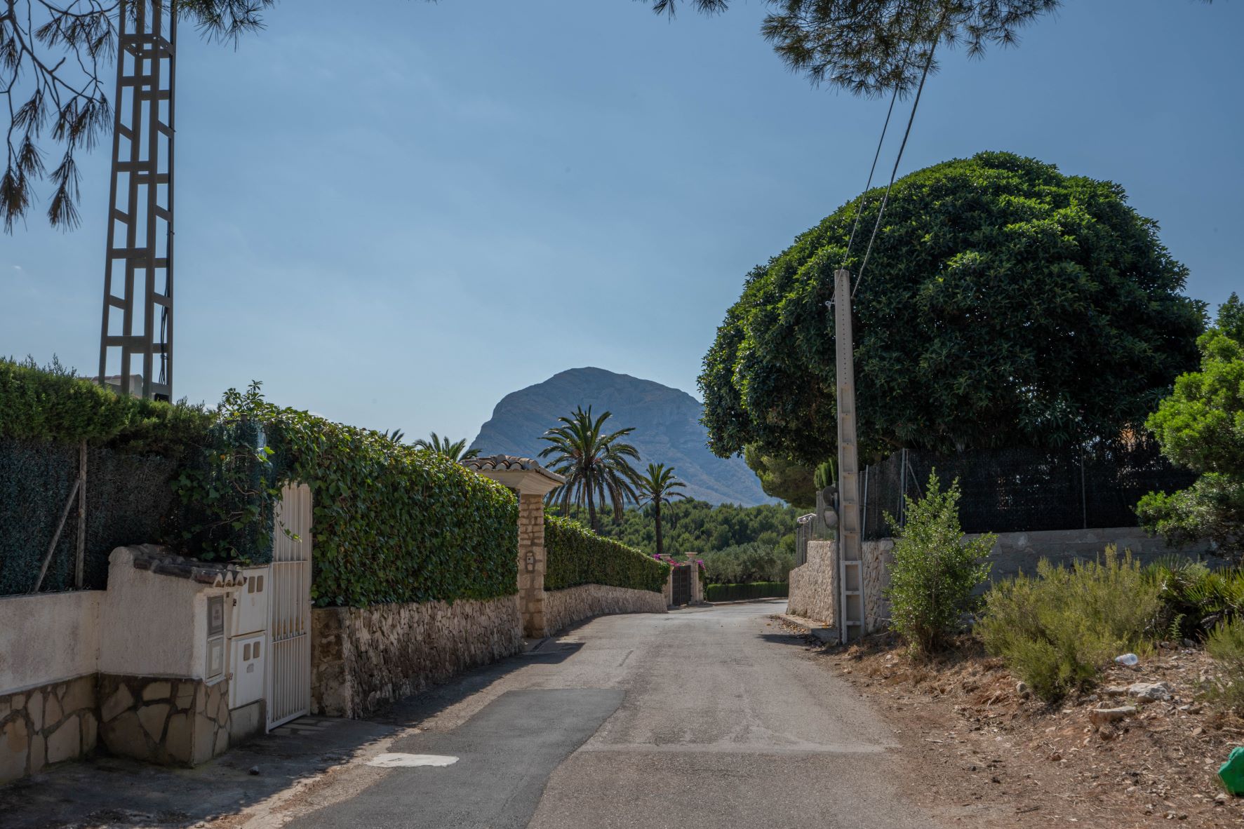 Street view framed by stone walls and lush greenery, with a striking mountain backdrop.
