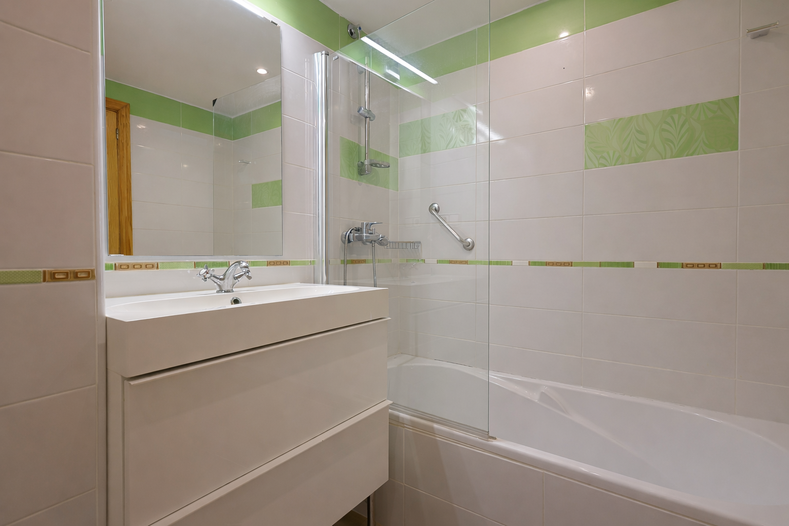 Bathroom featuring a modern sink, white tile with green accents, and a glass-enclosed shower.