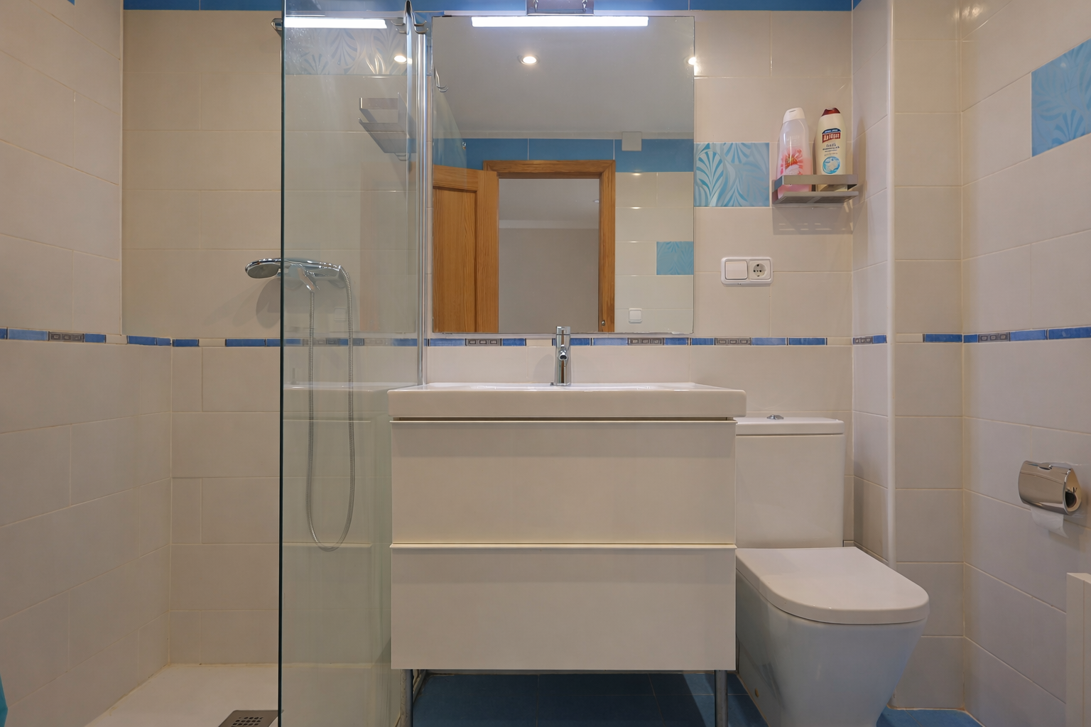 Bathroom with white tiles, blue trim, a mirror, modern vanity, and glass-enclosed shower.