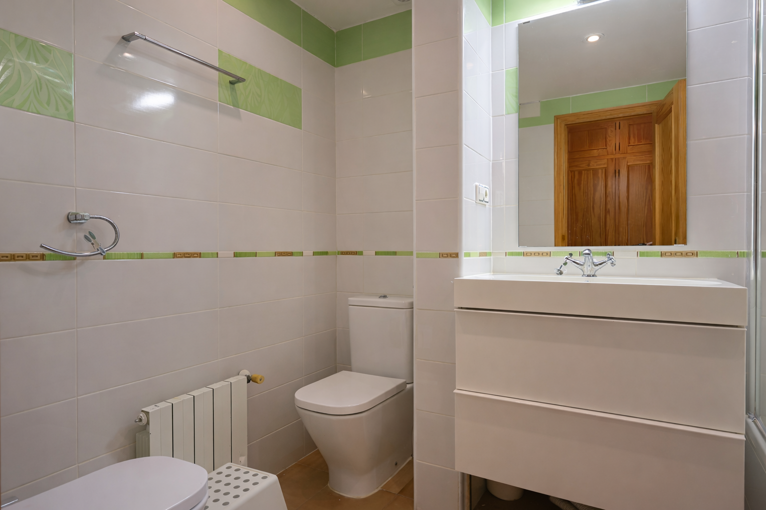 Bathroom with white tiles, green accents, modern sink vanity, and mirror.