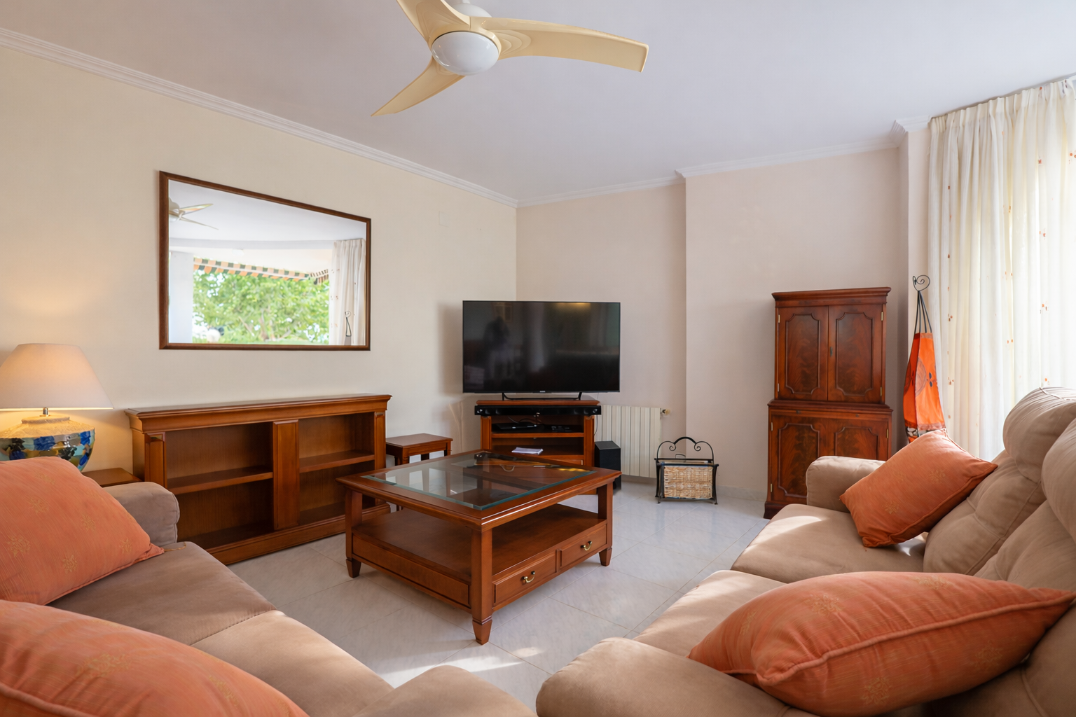 Bright living room featuring beige sofas, wooden furniture, and a mirror reflecting the outside.