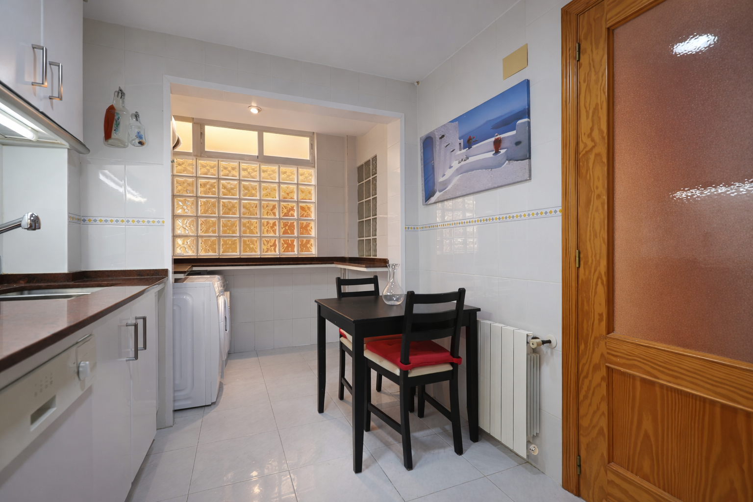 Functional kitchen features a dining table, white appliances, and a glass block window.