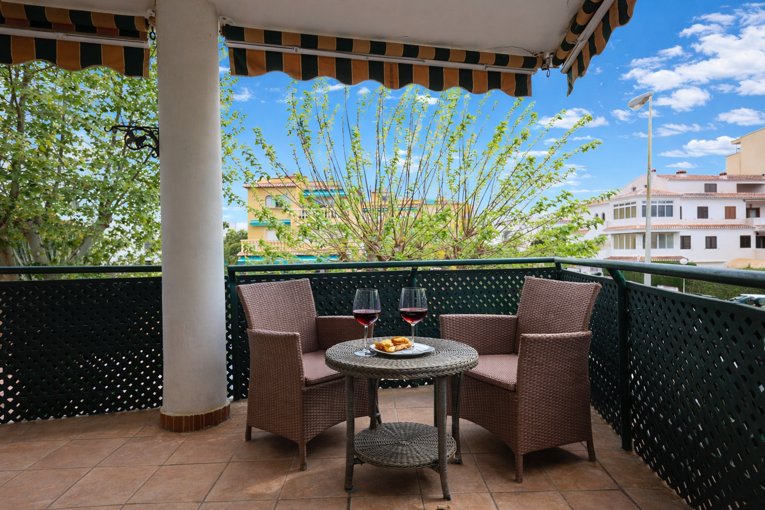 Tiled terrace featuring a striped awning and wicker furniture with outdoor views.