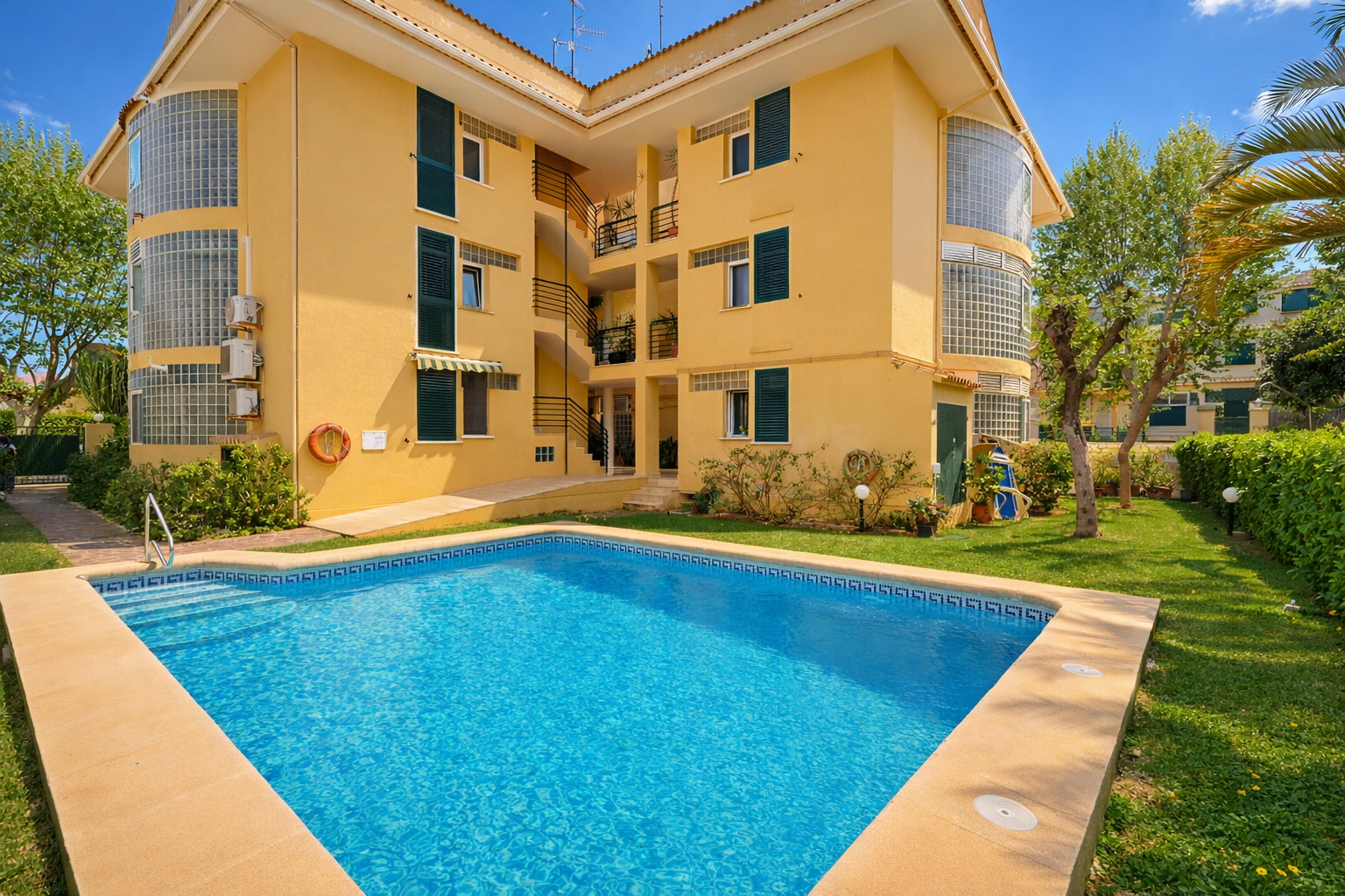 View of the building's communal pool with yellow facade and green shutters.