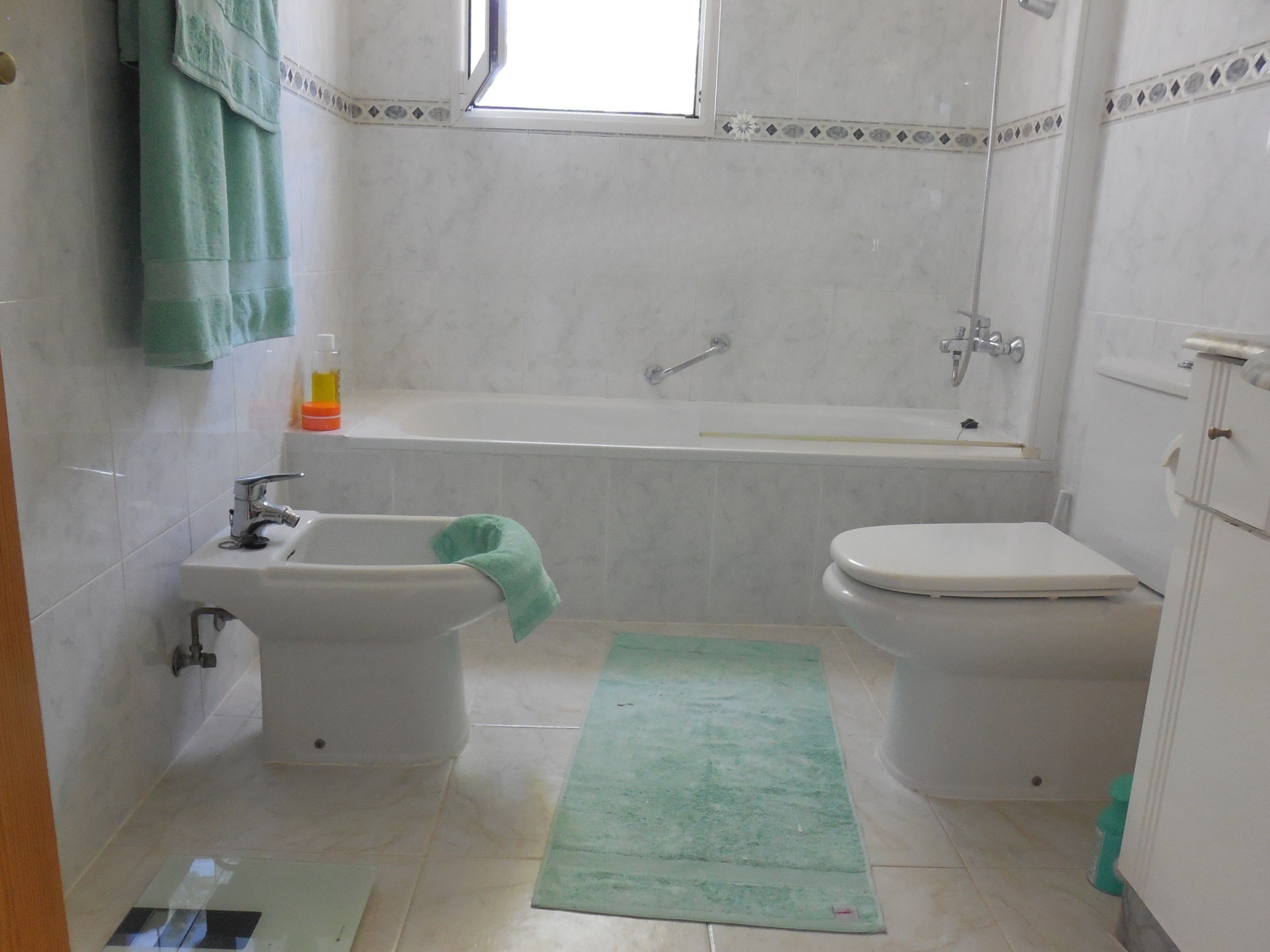 Bathroom featuring marble-like tiles, a bathtub, bidet and mint green towels.