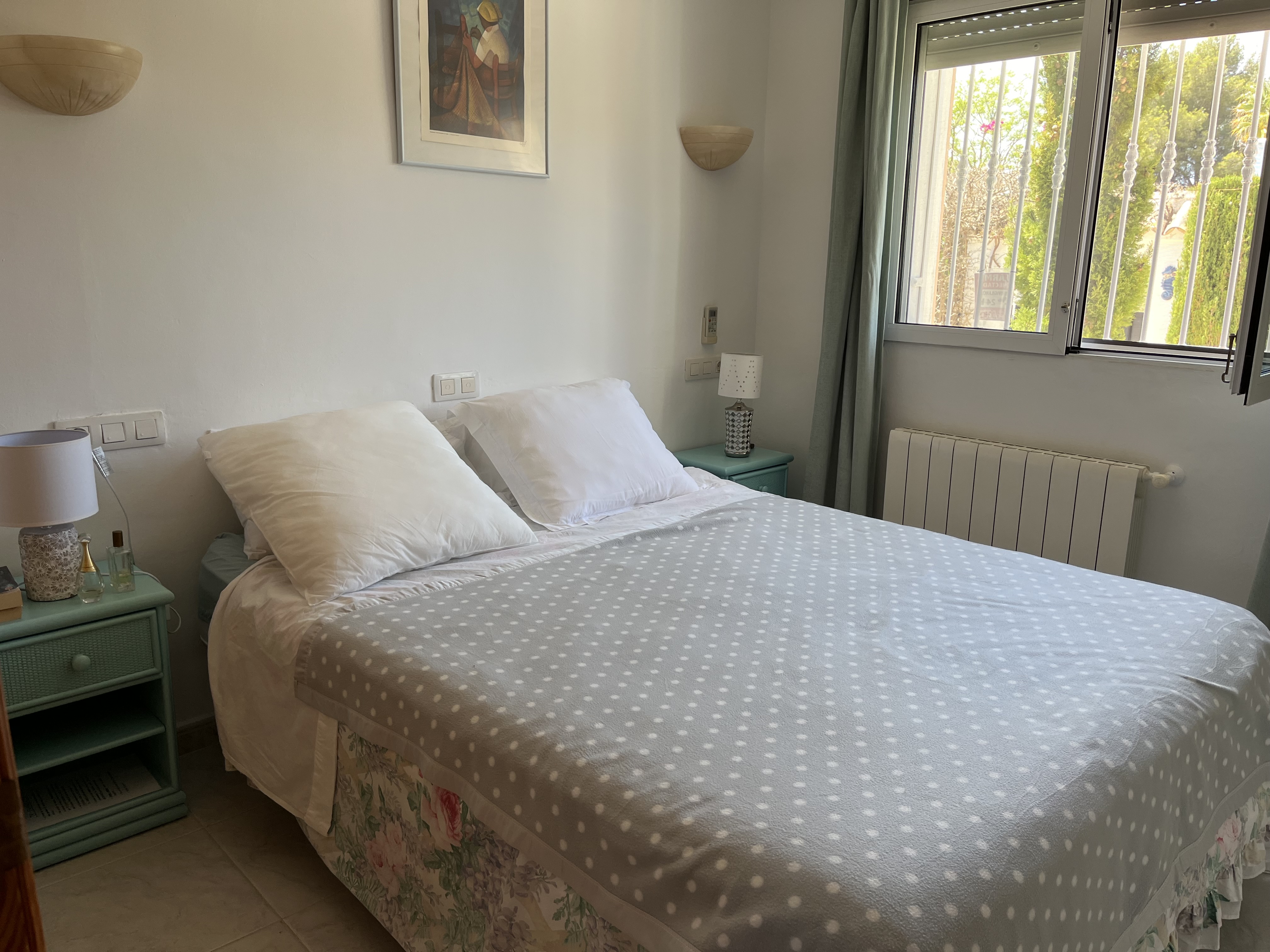 Bright bedroom featuring a double bed, turquoise nightstand, and decorative details.