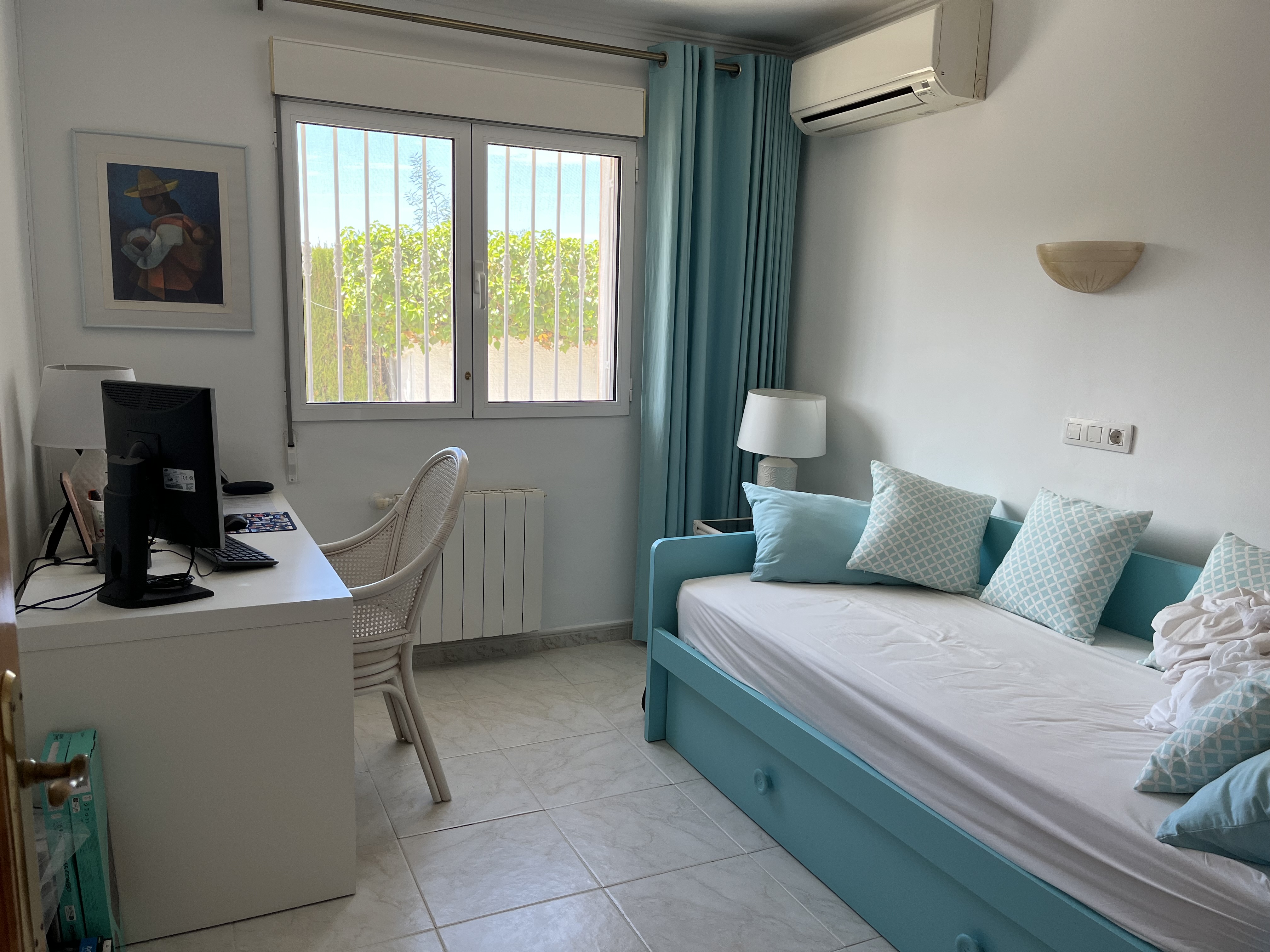 Bright bedroom with turquoise daybed, white desk, and garden view.