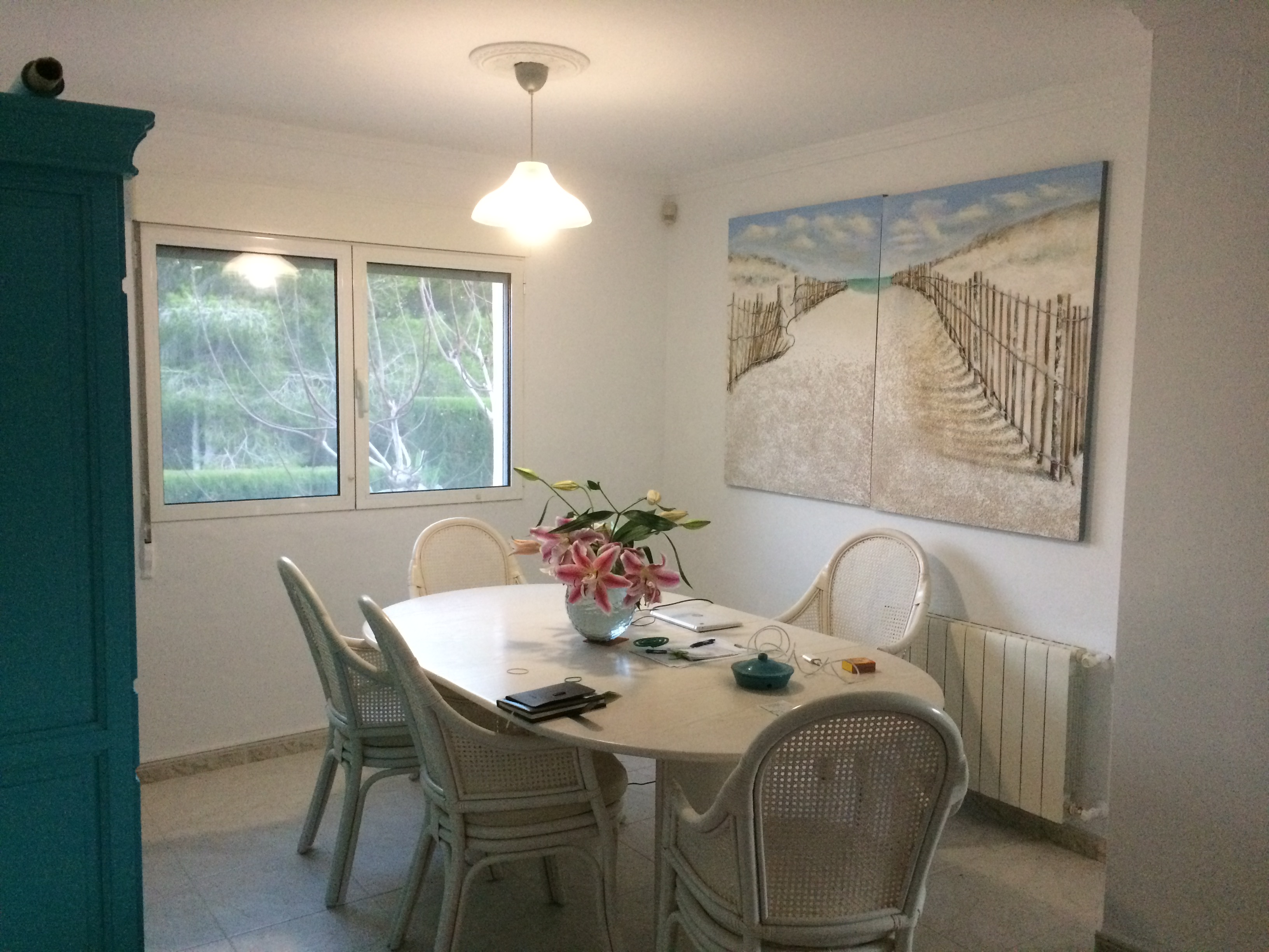 Bright dining room featuring an oval stone table, wicker chairs, and a beach-themed painting.