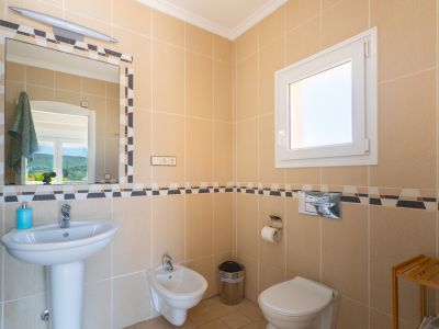 Bathroom detail with cream-colored tiles and decorative border. Includes pedestal sink, bidet, and toilet.