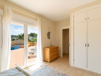 Bright bedroom featuring terrace access with pool view. Includes built-in wardrobe and wooden dresser.