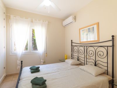 Bright bedroom featuring twin beds with wrought iron headboard and views to the outside through sheer white curtains.