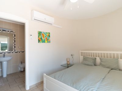 Bright bedroom with en-suite bathroom, decorated with a colorful painting and white wood bed.