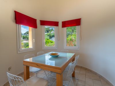 Bright dining area with a glass-top table and views through windows with red valances.