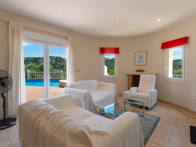 Bright living room with pool terrace access. White covered sofas and red accent details.