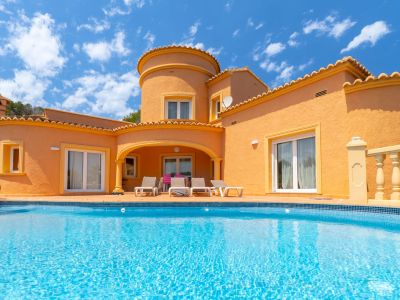 View of the main facade with turquoise pool and terrace with sun loungers.
