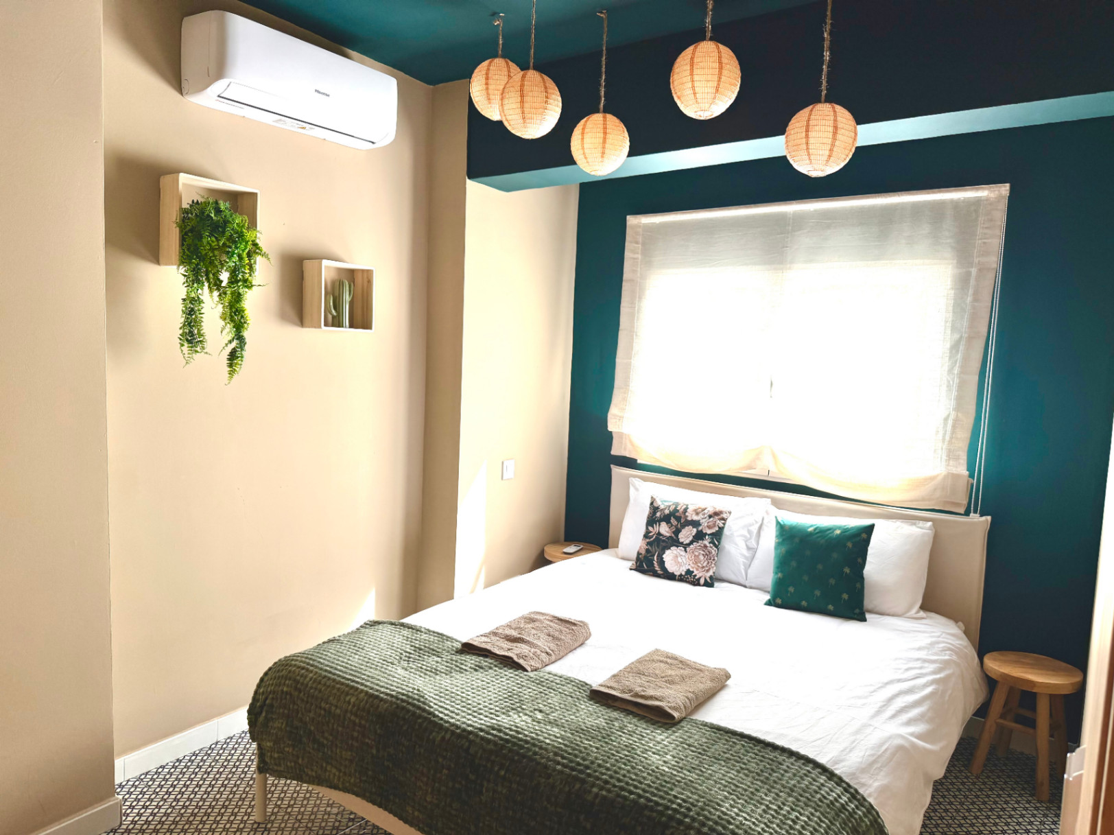 Bedroom featuring cream walls and teal accents. Hanging lights and minimalist decor create a cozy space.