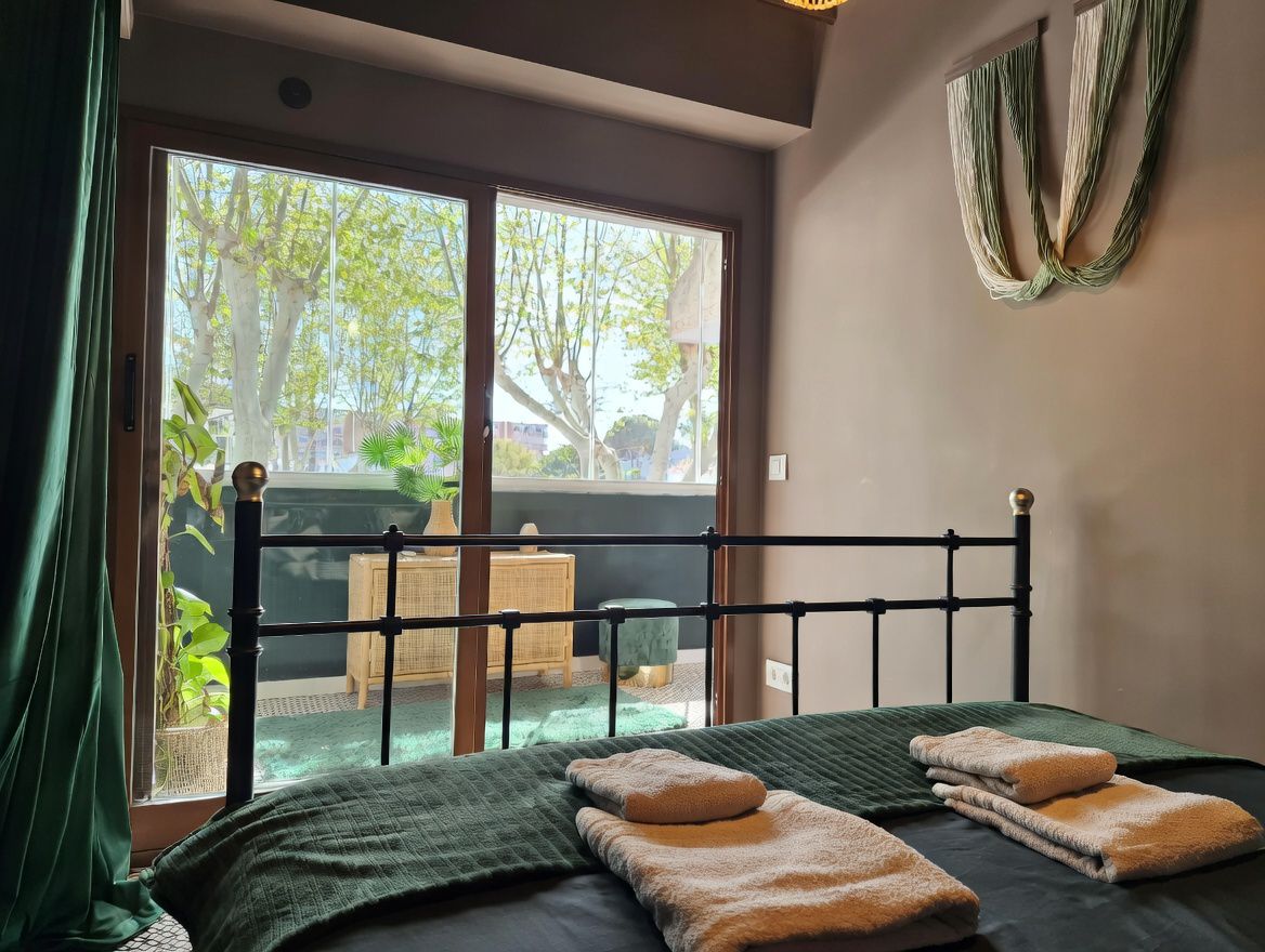 Bedroom with wrought iron bed, balcony with tree-lined views, and modern decor in neutral and green tones.