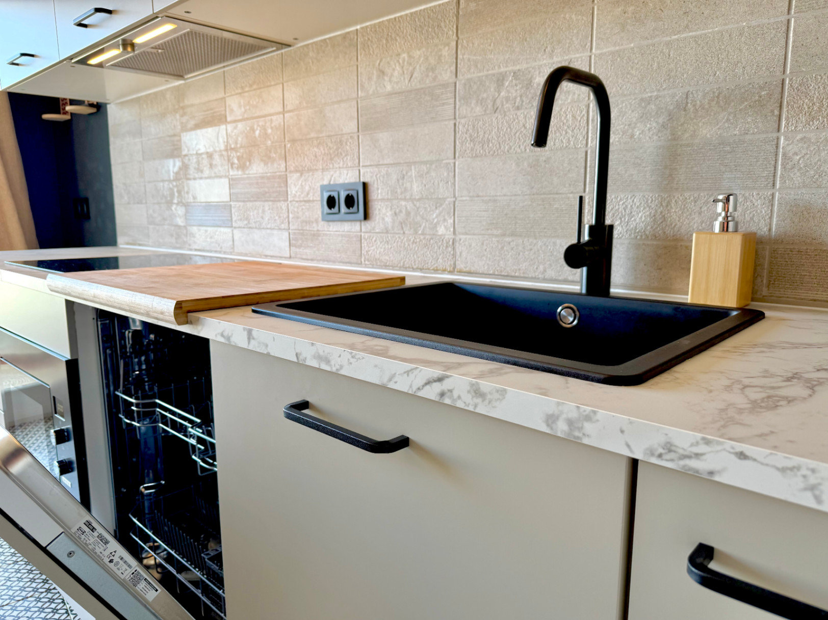 Close-up of the renovated kitchen featuring a black sink, marble countertop, and textured tile backsplash.
