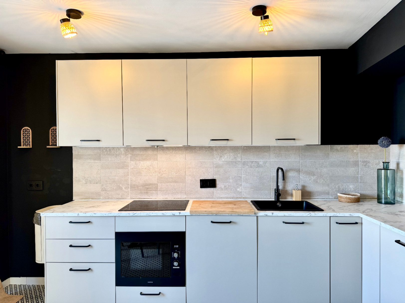 Close-up of the renovated kitchen featuring a marble countertop, light cabinets, and a contrasting black wall.