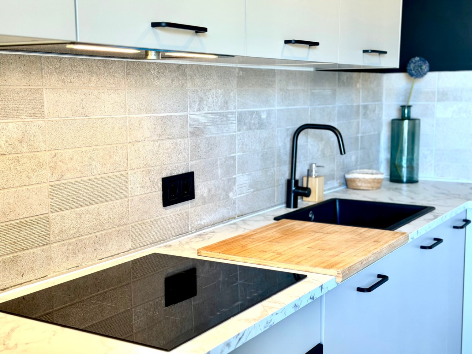 Detail of the renovated kitchen with marble countertop, black sink, and induction hob.