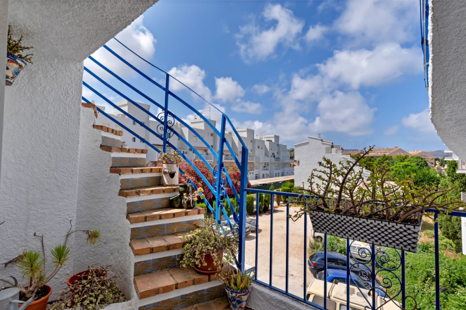 Exterior staircase with blue railings and floral details, leading to a terrace overlooking the parking area.