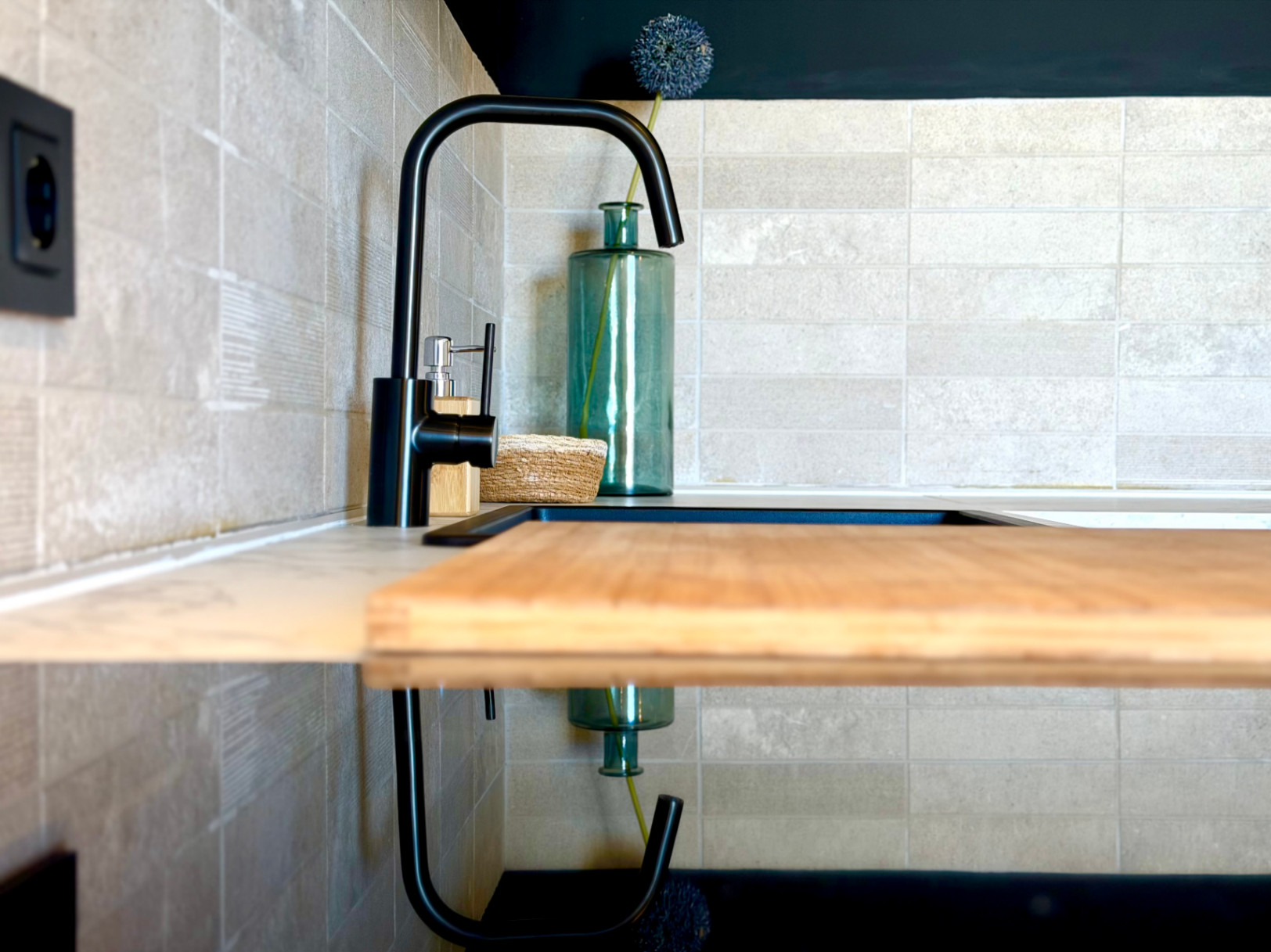 Kitchen detail with black faucet, wood cutting board, and textured ceramic tile backsplash.