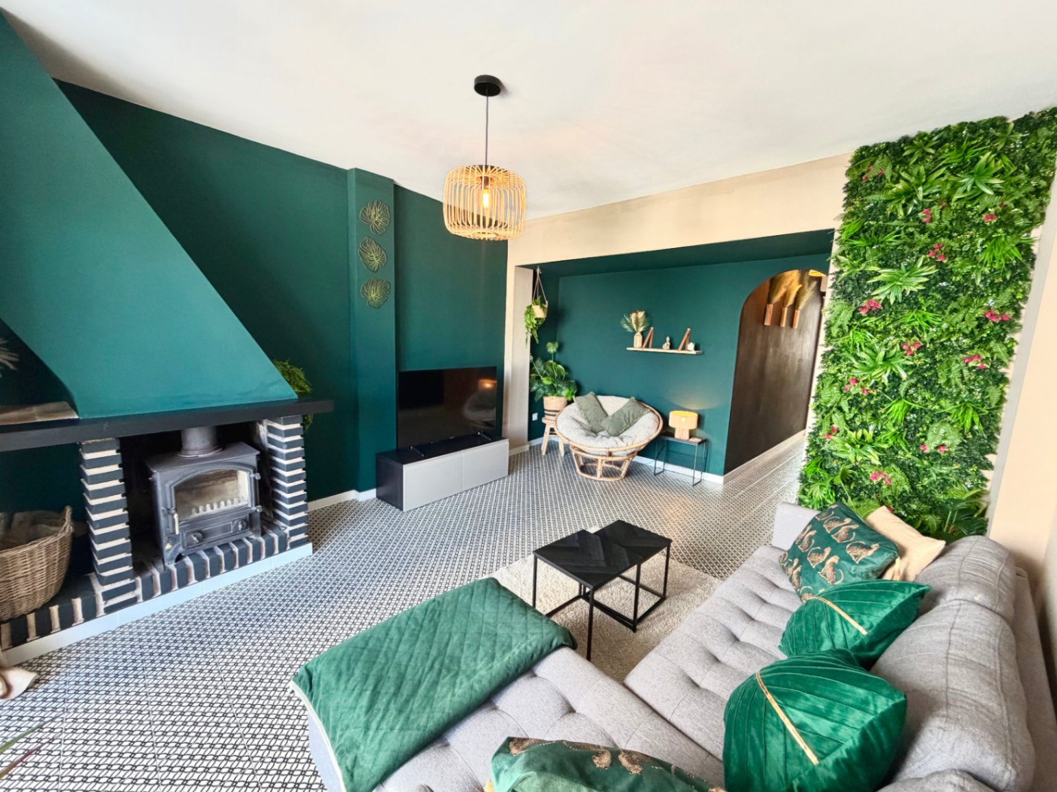 Living room featuring a rustic fireplace, green wall accent, geometric floor tiles, and a wicker pendant light.