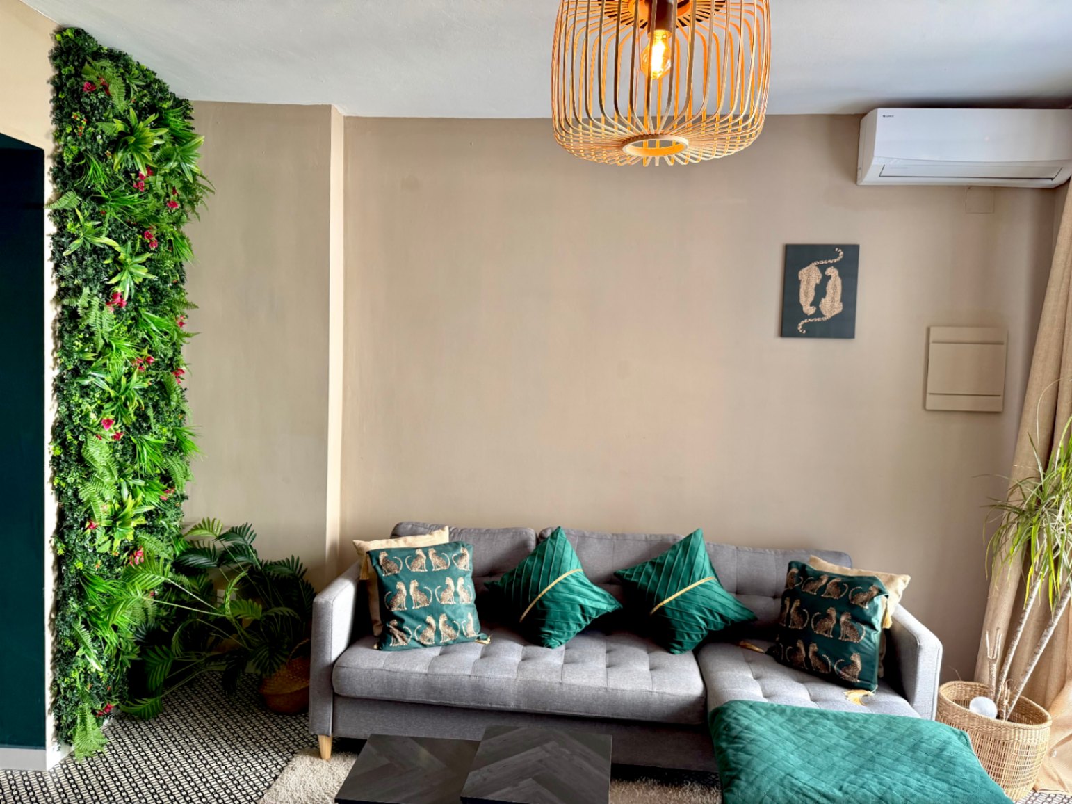 Modern living room with a vertical green wall, a gray sofa with green cushions, and a wooden ceiling lamp.