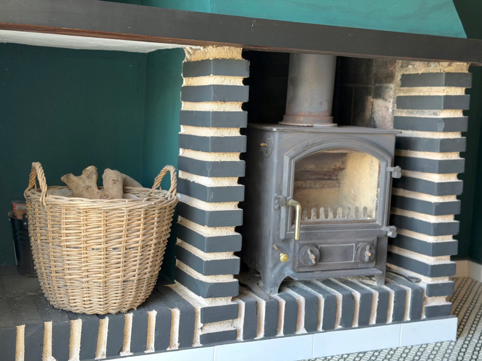 Rustic fireplace with painted brick details and a woven wicker wood basket.