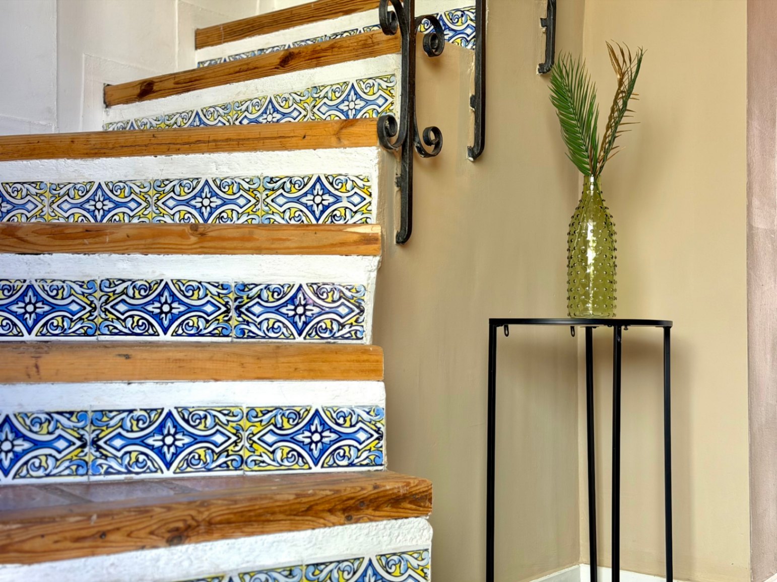 Staircase detail with decorative tiles and wrought iron railing. Green vase with plant.