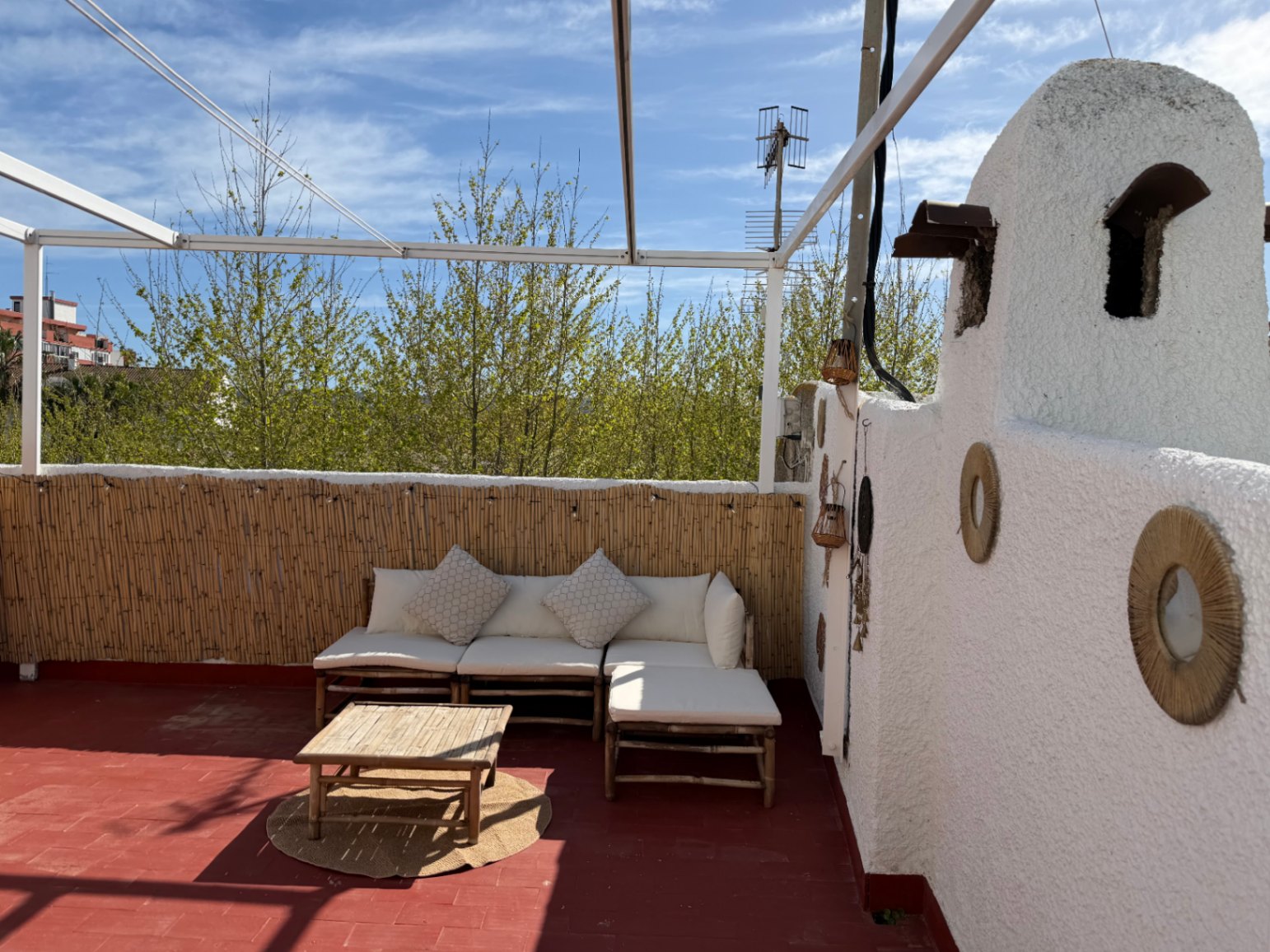 Terrace with red floor, bamboo seating and a white wall decorated with esparto circles.