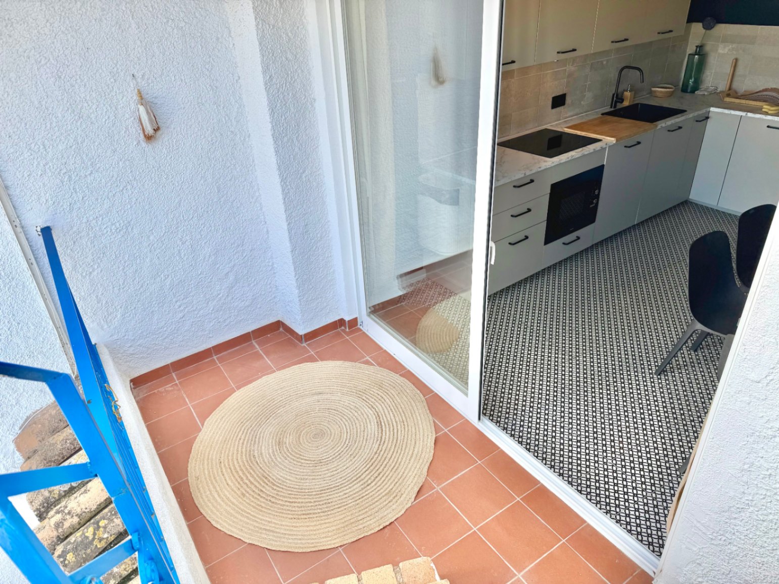 Terrace with terracotta flooring and access to a modern kitchen with black and white geometric flooring.