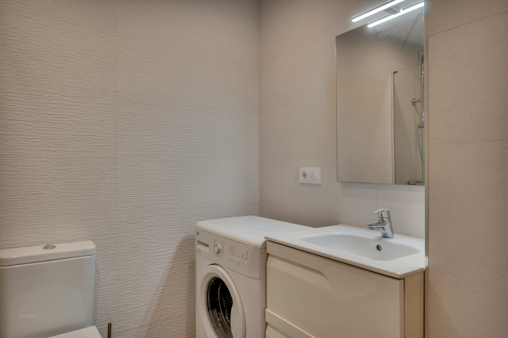 Bathroom detail with built-in sink, washing machine, and textured walls in neutral tones.