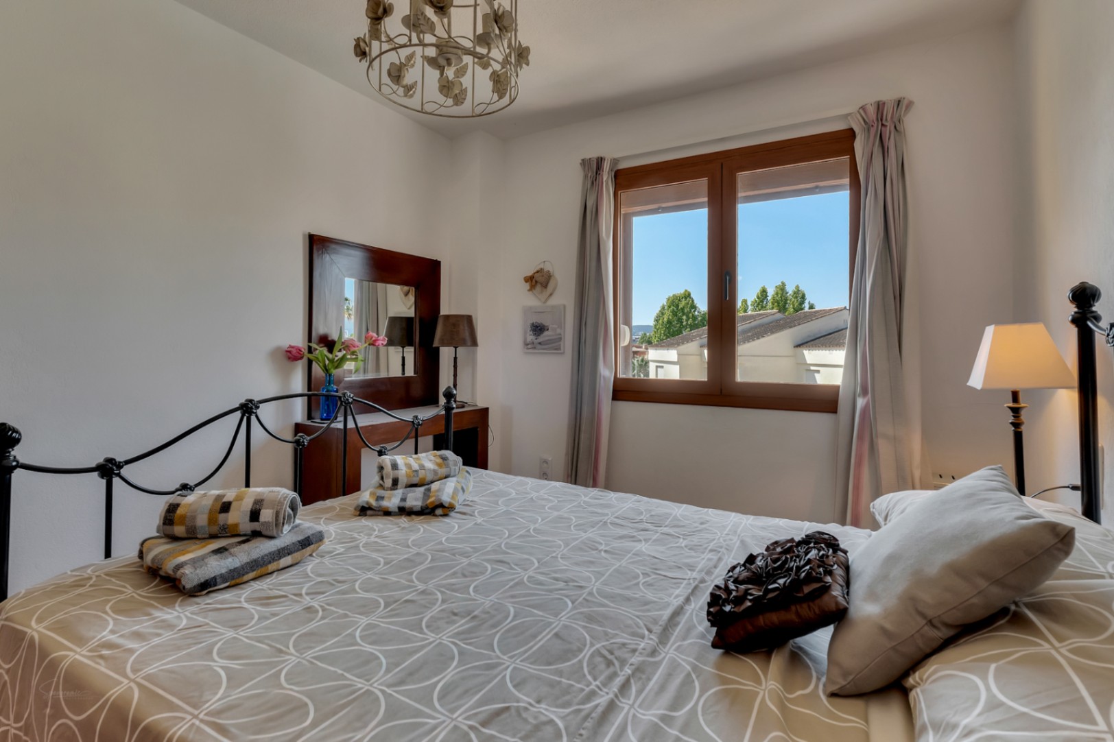 Bright bedroom featuring a wrought iron bed, patterned bedding, and a wood-framed window with exterior views.