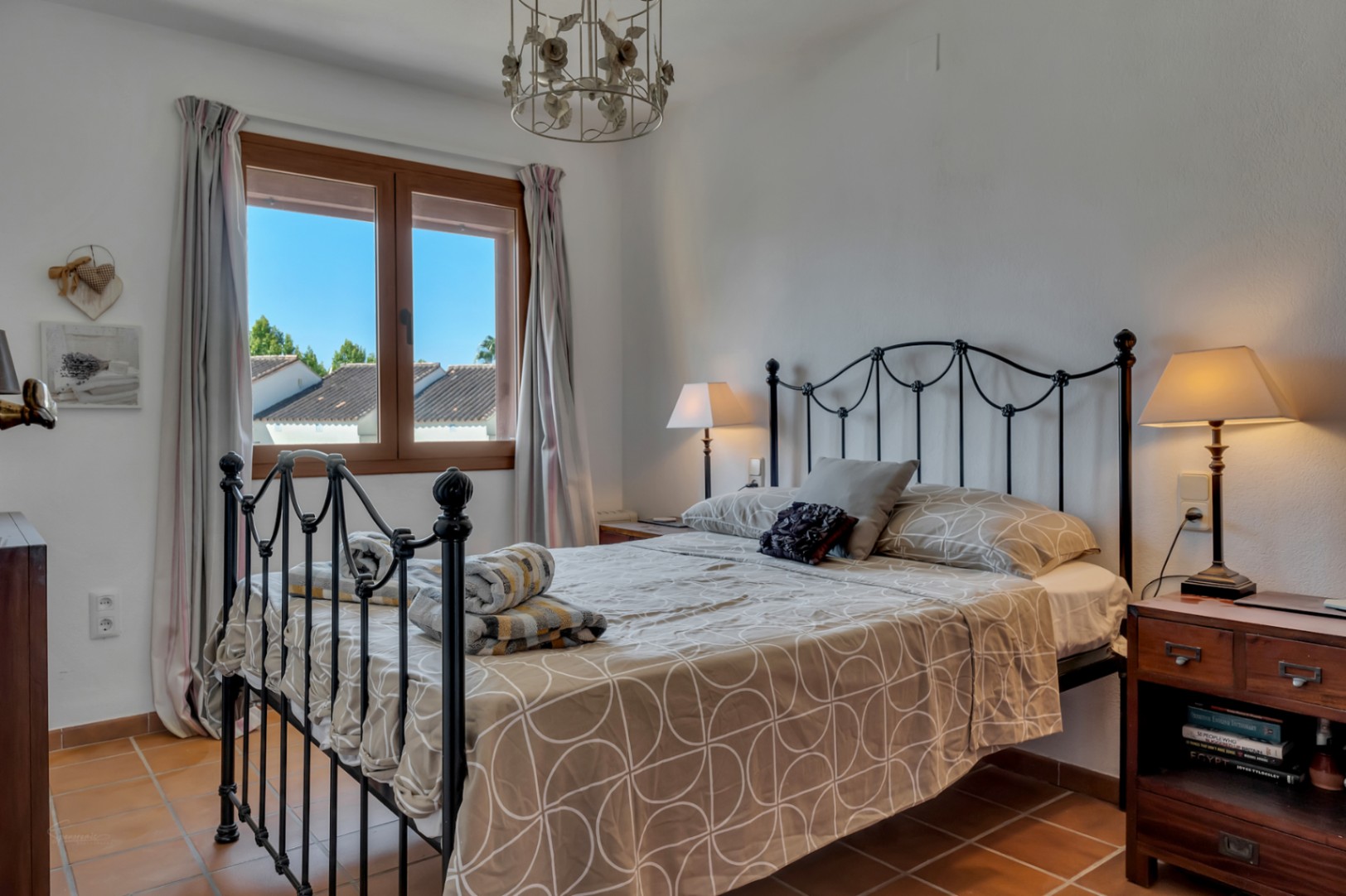 Bright bedroom with wrought iron bed, window with exterior views, and terracotta flooring.