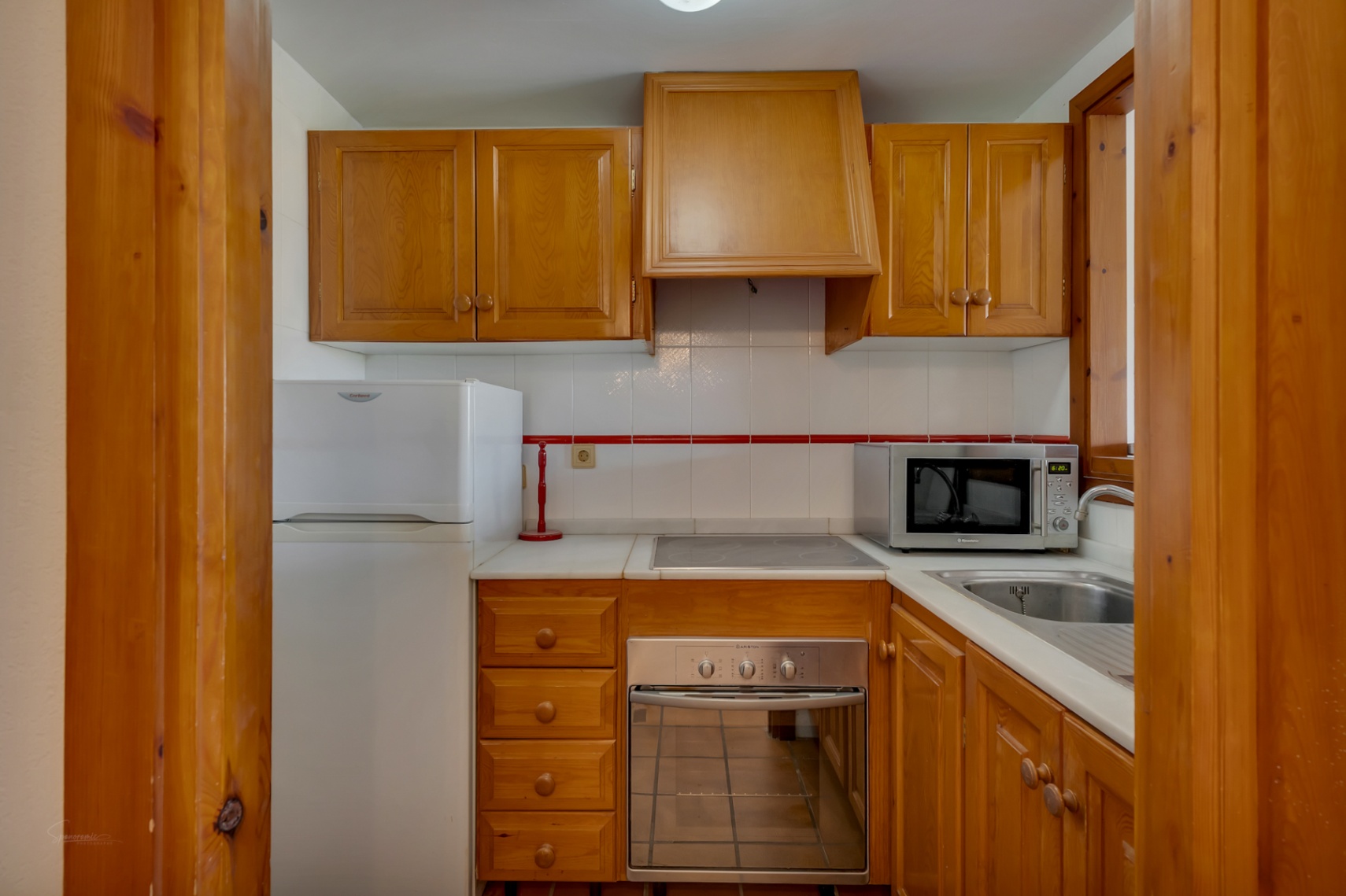 Compact kitchen with wood cabinetry, white appliances, and light countertop.