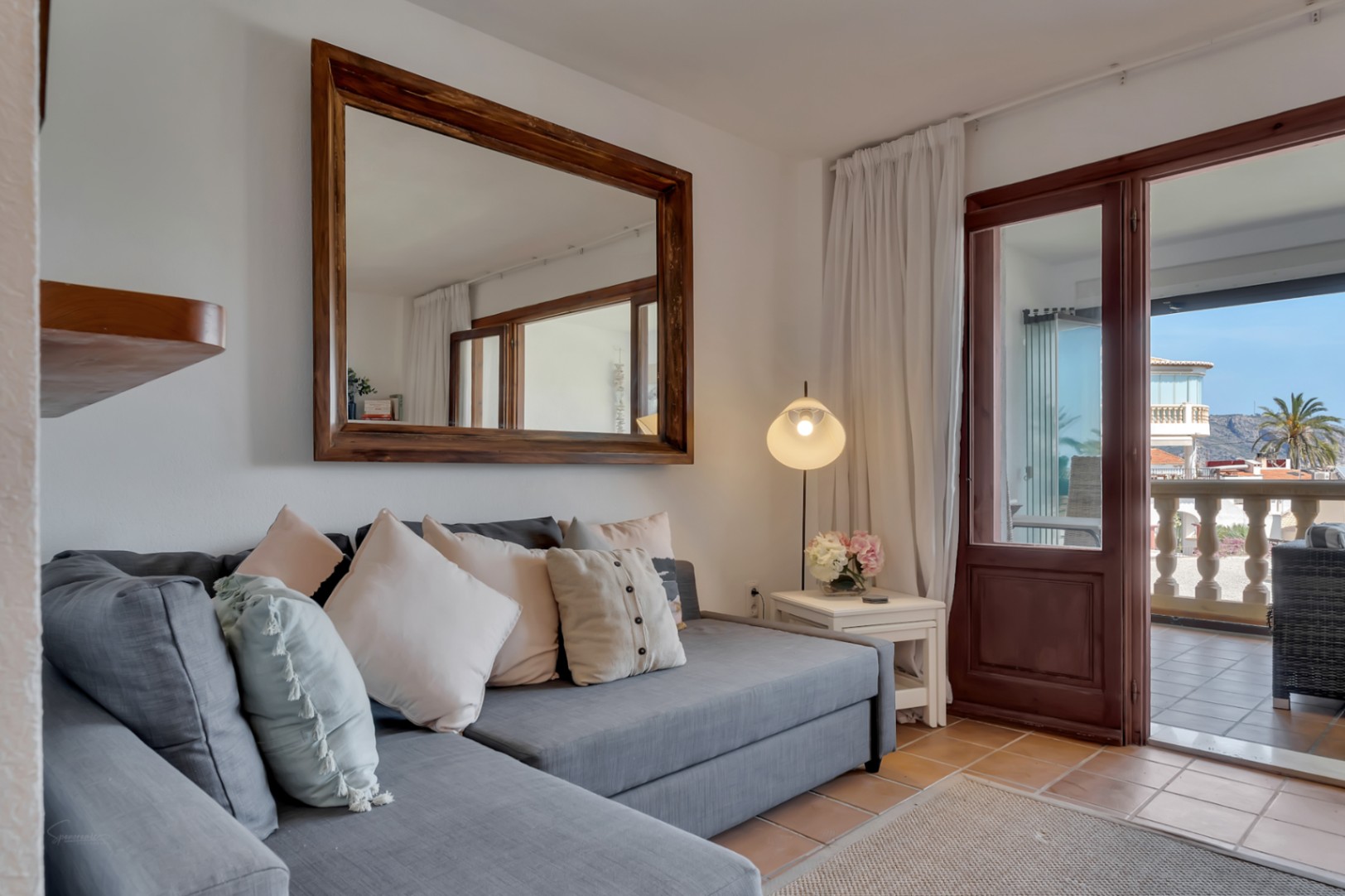 Living room featuring a modular gray sofa, wood-framed mirror, and terrace access with views.