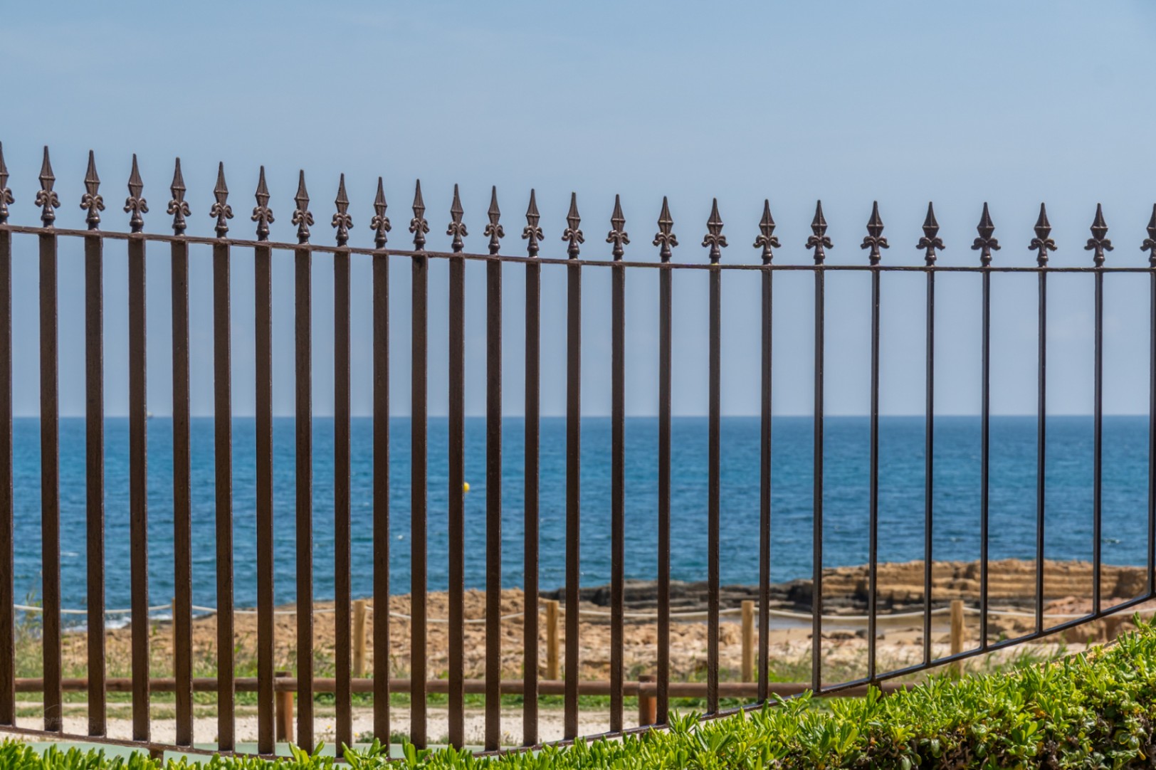 View of the Mediterranean through an ornamental iron railing with greenery in the foreground.