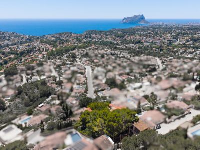 Aerial view of a coastal residential area with the Mediterranean Sea and Peñón de Ifach in the distance, under a clear blue sky.