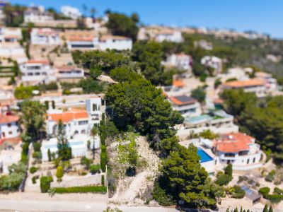 Aerial view of the Montemar urbanization in Benissa, featuring white villas with terracotta roofs and private pools nestled on a green, terraced hillside.