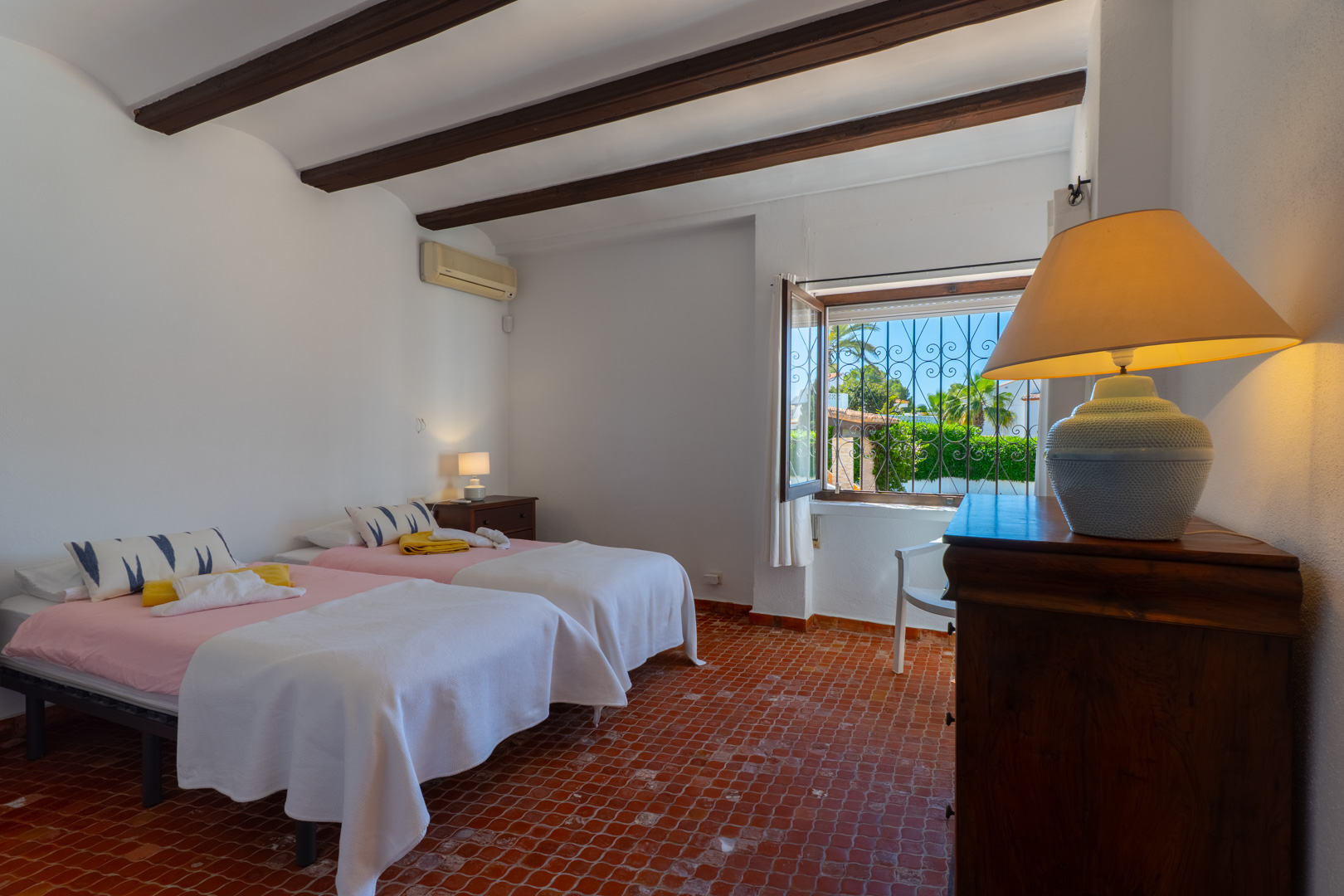 Bedroom with twin beds, wood beams, and terracotta tile floor. Exterior views.