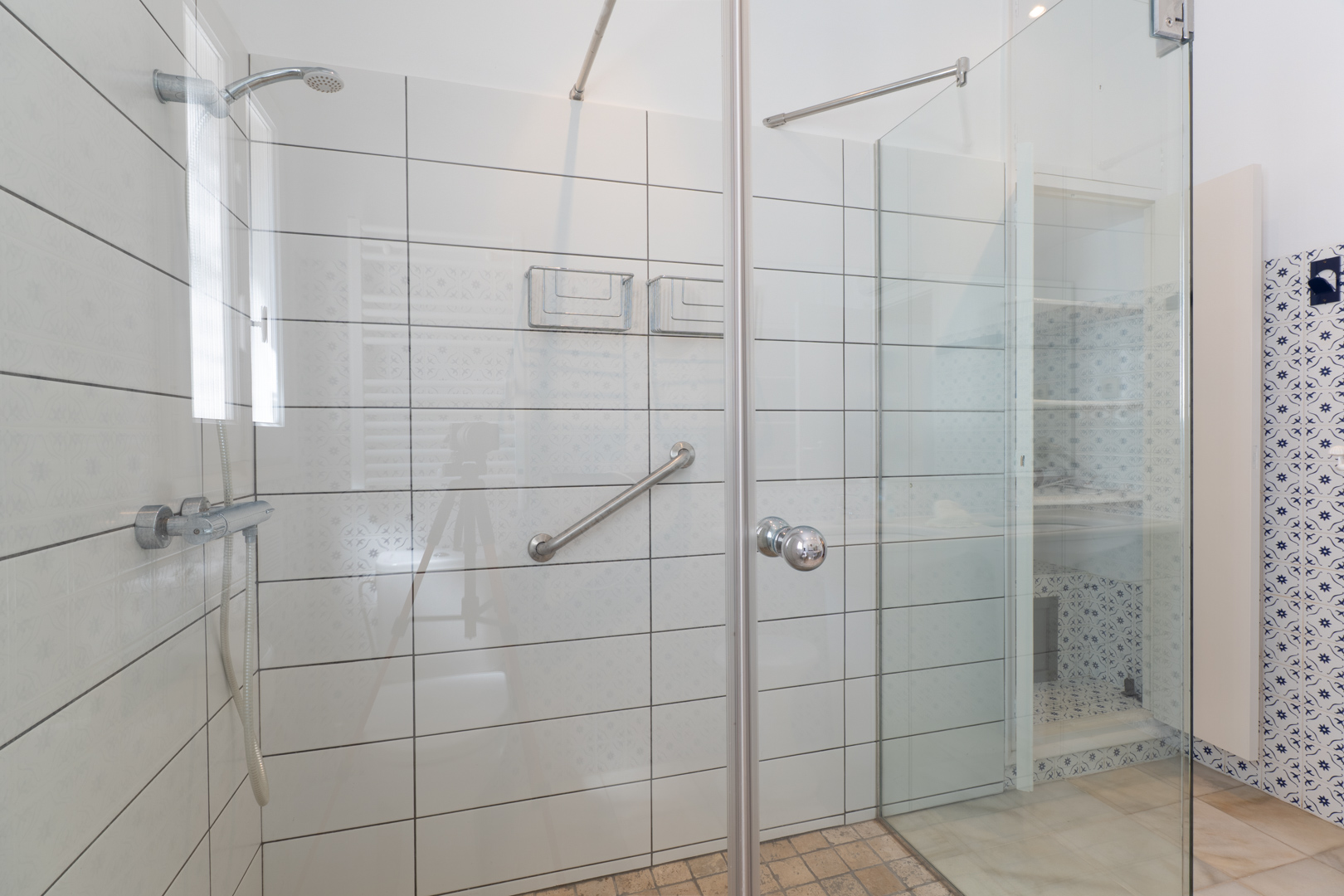 Close-up of the shower with glass enclosure and white tiles with subtle patterns.