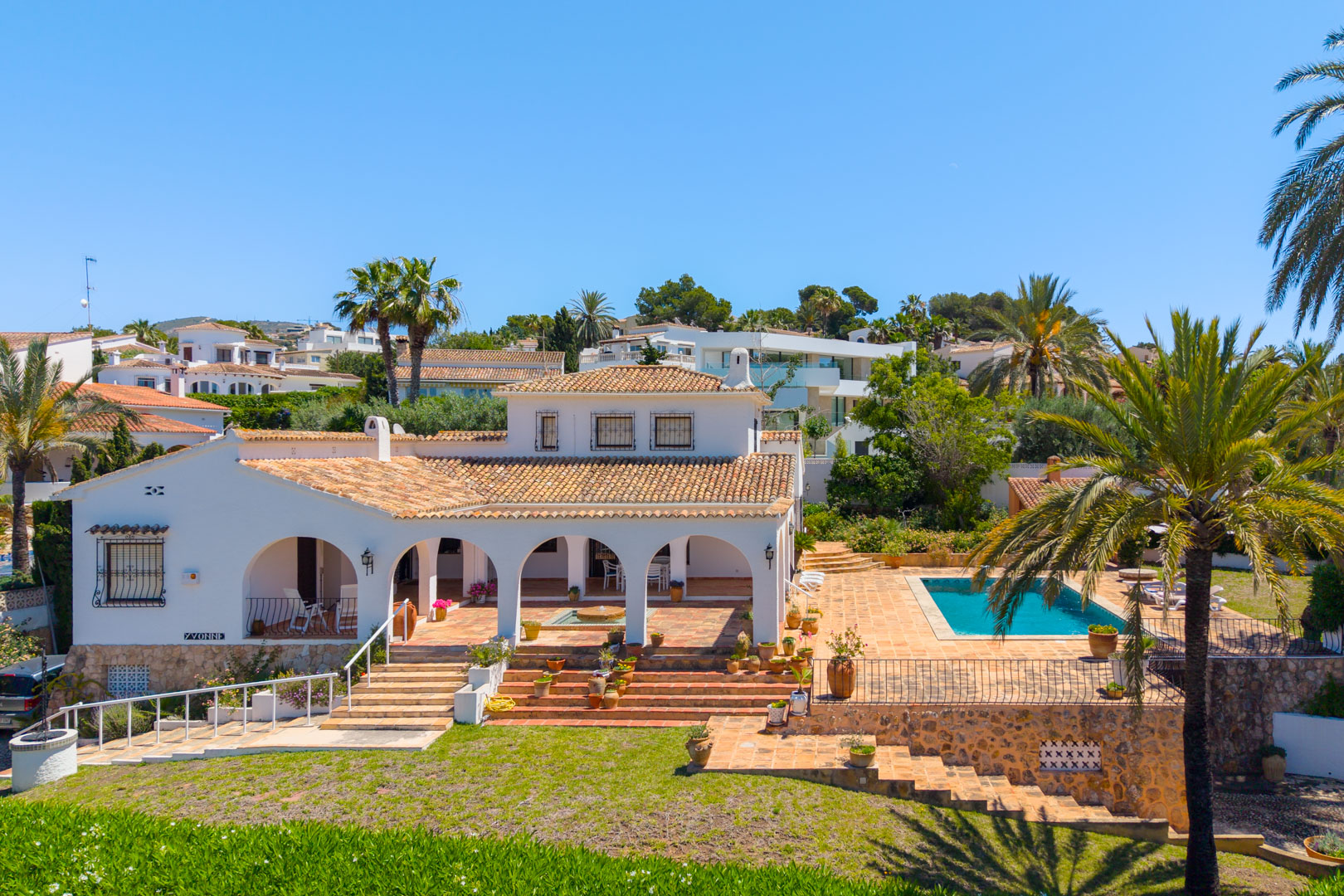 Elevated view of the villa featuring arches, a pool, and a tiered garden with greenery.
