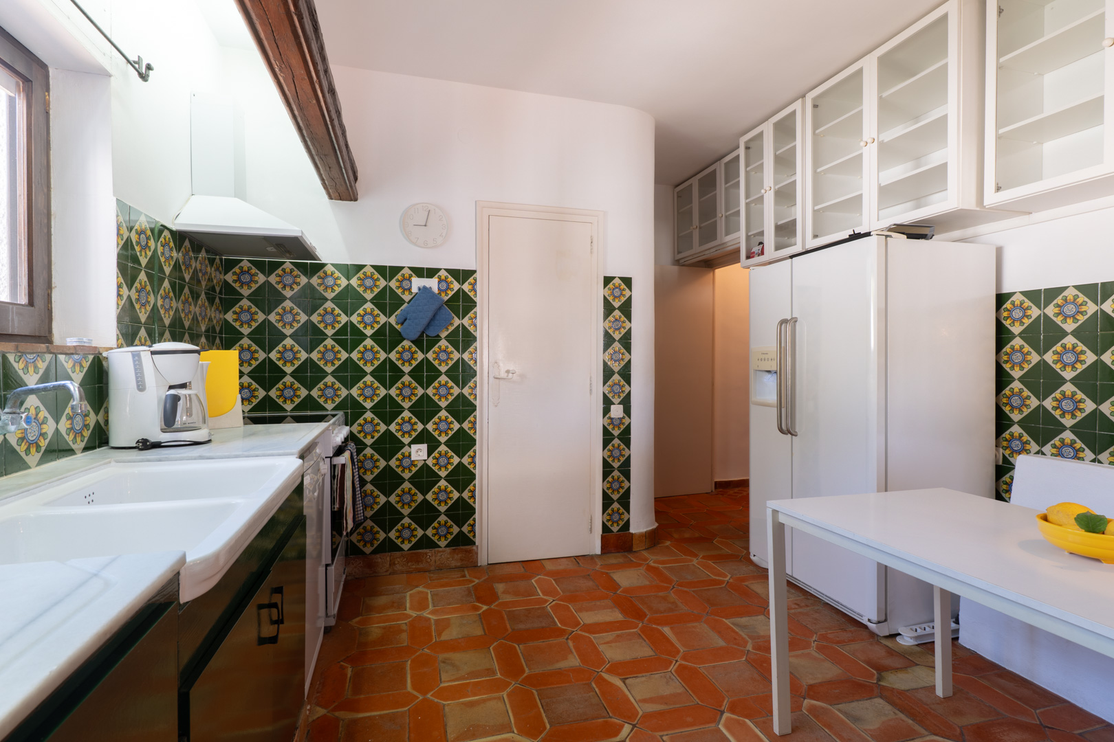 Kitchen featuring decorative tiles, terracotta flooring, and white upper cabinets.