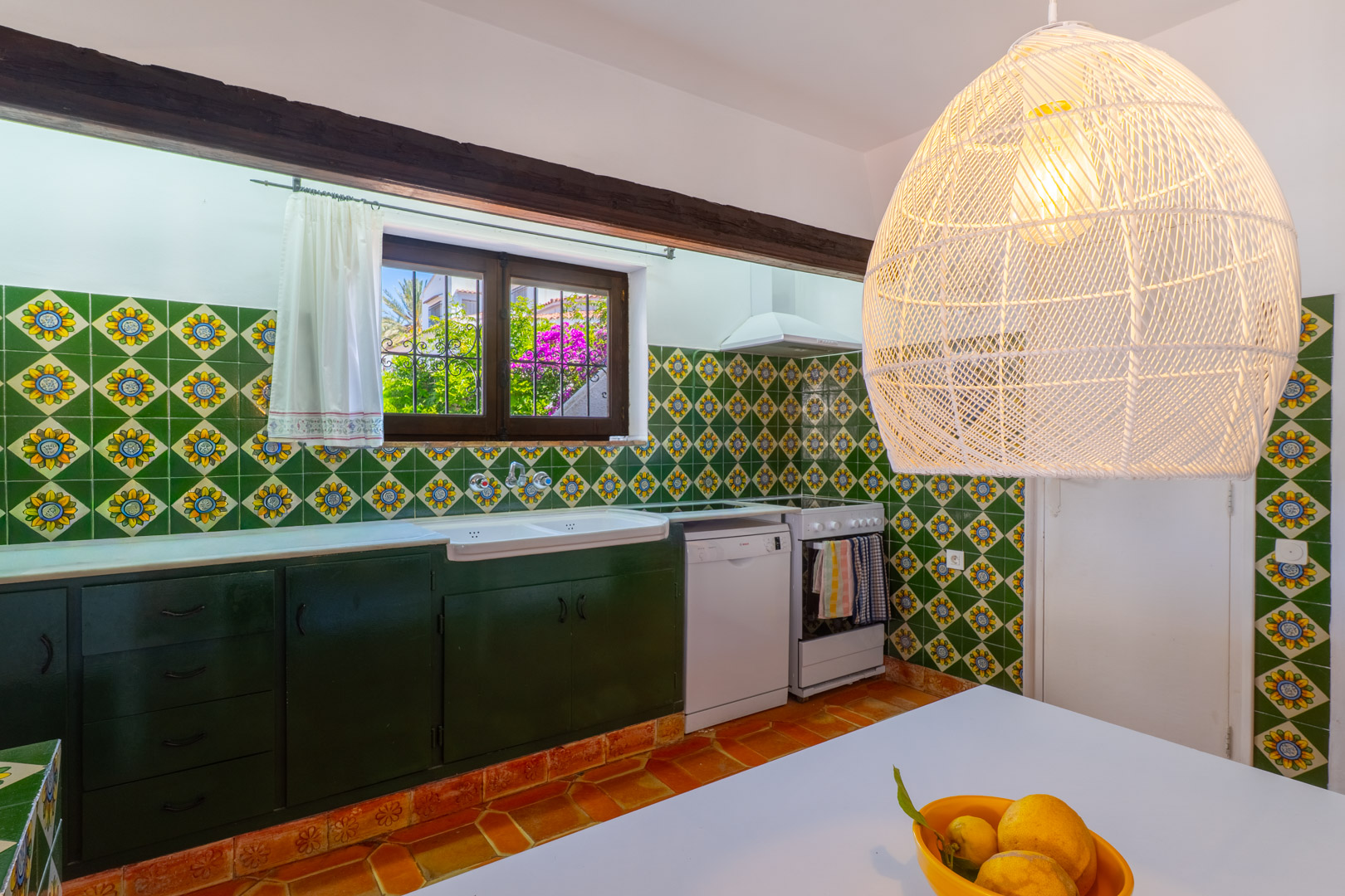 Kitchen with decorative tiles, dark green cabinets, and a woven pendant lamp.
