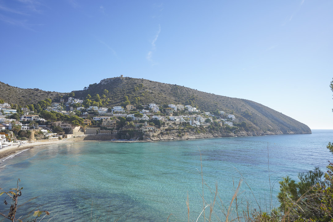 Panoramic view of Moraira's coastline with turquoise waters and white houses on the hillside.